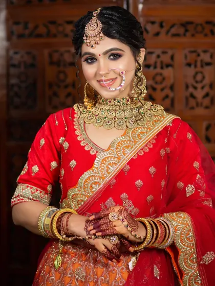 A smiling bride ready for her wedding. The makeup is a perfect balance of traditional and modern, with a classic red and orange lehenga complemented by soft, glowing makeup.