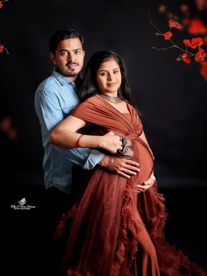 The couple holds a pair of tiny baby shoes together over the bump. This close-up shot against a dark background is full of emotion and anticipation.
