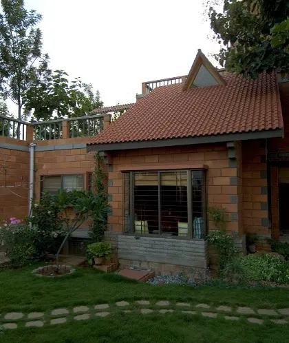 The Sharada Residence, with its sloping tiled roof and integration with the garden, evokes the charm of a traditional cottage. The design prioritizes a human scale and a strong connection to the natural surroundings.