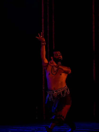 A solo portrait of me during a Mayurbhanj Chhau performance, captured under dramatic red and blue lighting.