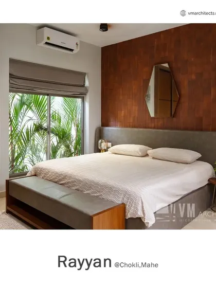 A bedroom in Rayyan with a warm, wood-tiled accent wall and a large window dressed with roman blinds, offering a view of the lush outdoor plants.