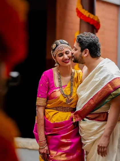 A sweet kiss on the cheek. This candid shot captures the affection and joy between the couple in their colorful South Indian wedding attire.