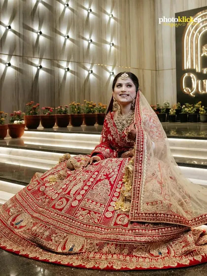 A joyful portrait of the bride seated, her magnificent red lehenga spread around her, showcasing its detailed craftsmanship.