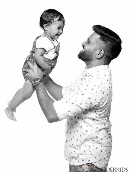A black and white portrait capturing the joy of a father lifting his child into the air. The simple background puts all the focus on their happy expressions and connection.