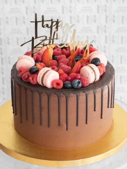A rich chocolate drip cake topped with a vibrant mix of fresh berries and pink macarons.