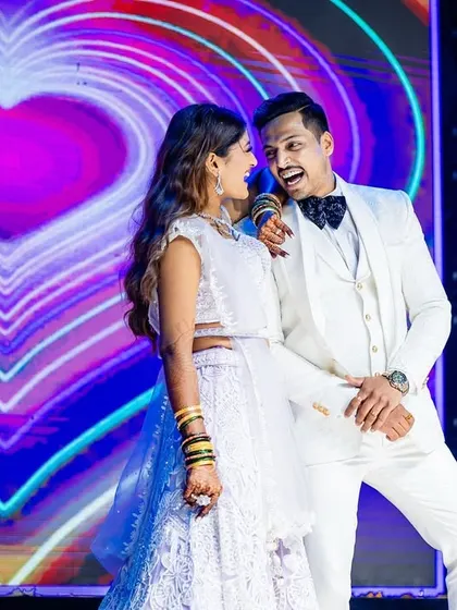 The couple shares a microphone during a fun performance, with a heart-themed LED screen in the background.