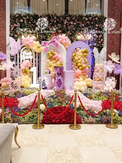A wider view of the butterfly garden stage, showcasing the neon "One" sign and the beautiful blend of floral arrangements and balloon art.
