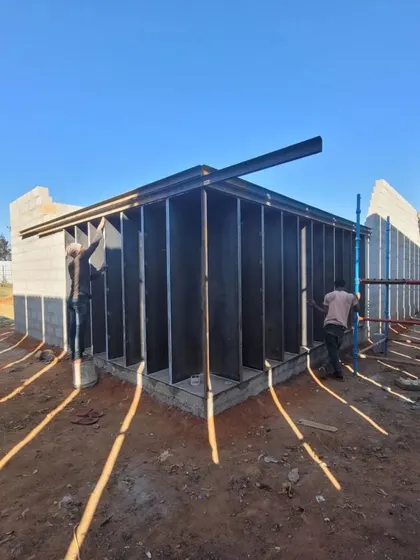 Workers install the structural framework of the gallery. The morning light casts long shadows, highlighting the rhythm of the vertical fins that will define the building's facade.