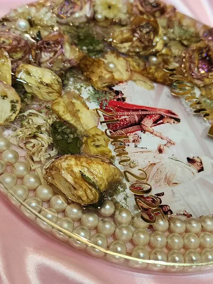 A close-up of the details on an oval varmala preservation plaque. I carefully place each dried flower and pearl to create a balanced and beautiful composition around the couple's photo.
