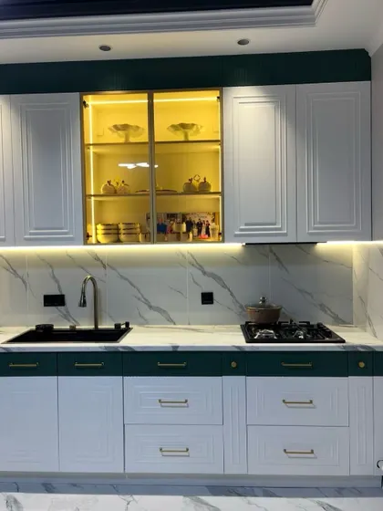Another view of the green and white kitchen, highlighting the illuminated glass crockery unit and the clean lines of the countertop area.