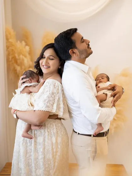 An identical pose to the hero shot, this image offers a slightly different emotional beat. The parents stand back to back, each holding a newborn twin, in a moment of peaceful contentment.