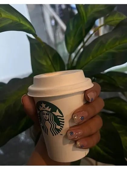 A trendy and protective evil eye design. These short, natural-looking nails are adorned with tiny, detailed evil eye art and flecks of gold foil.