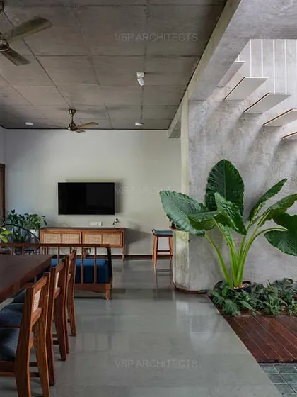 Inside 'HAVEN', an open-plan living and dining area features a raw concrete ceiling and a striking floating staircase, with indoor plants blurring the line between inside and out.
