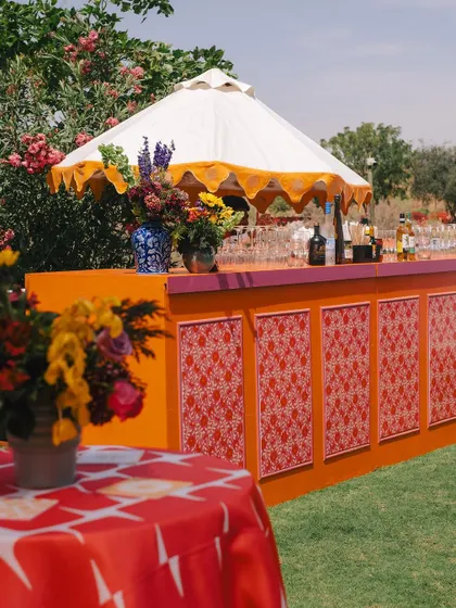 The bar front features intricate red and white printed panels, sheltered by a traditional Indian umbrella with a yellow scalloped edge.