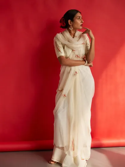 A full-length shot that captures the grace and elegance of the entire ensemble. The red background provides a powerful contrast to the white saree.