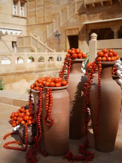 Terracotta pots filled with tomatoes and garlands of red beads, a rustic and earthy decor element.