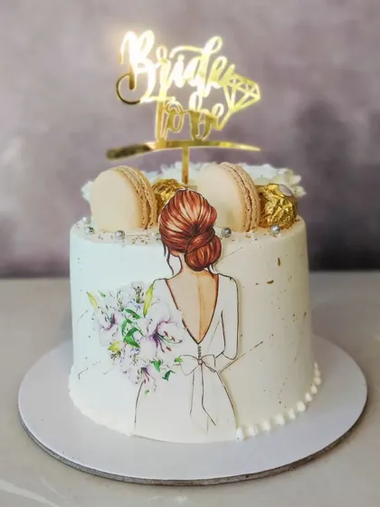 An elegant and modern cake for a bride-to-be. This custom cake features a beautiful hand-painted illustration, macarons, and a stylish "Bride to Be" topper, all without fondant.