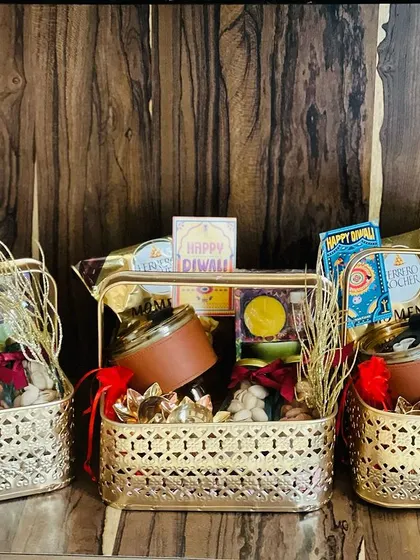 A set of three ornate golden baskets filled with a variety of Diwali treats and decor, perfect for a family or office team.