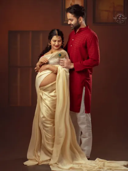 A tender moment between a couple in traditional wear, with the partner gently touching a peacock feather to his wife's shoulder.