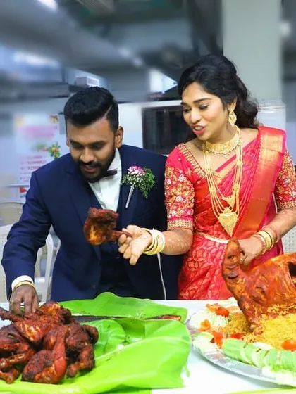 The bride and groom with their magnificent Raja Virundhu spread, featuring a whole roasted chicken on biryani and a platter of fried chicken.