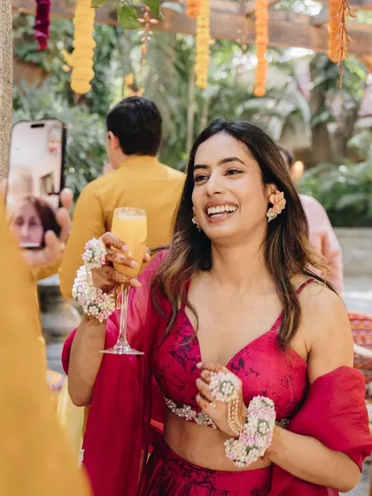 A candid shot of the bride enjoying her Haldi ceremony. The floral jewelry and bright pink outfit create a fresh and modern look.