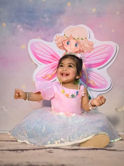 Dressed as a little fairy princess for her cake smash session. The setup includes a whimsical backdrop and props that match her sparkly dress, creating a magical scene for her birthday photos.