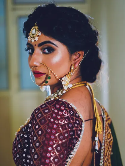A captivating bridal portrait by one of our students. The focus is on the dramatic eye makeup and the traditional nose ring, set against a rich, embroidered blouse, showcasing advanced makeup application skills.