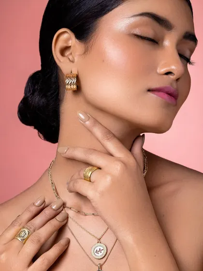 A close-up on the details: the texture of the gold earrings and rings, and the flawless, glowing skin.