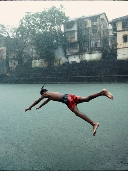 A boy in mid-air, diving into the waters of Banganga Tank during a rainstorm. This action shot captures the energy and tradition of this unique location, where the monsoon is a time for celebration and play.