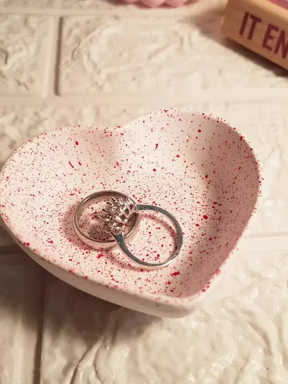 Our mini heart dish with a red splatter finish, holding a pair of rings. It's a perfect little spot on a bedside table to keep your jewelry safe overnight.