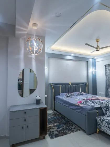 A chic master bedroom in blue and grey, featuring a stylish upholstered bed and a compact dresser with an oval mirror. The spherical pendant light adds a modern touch.