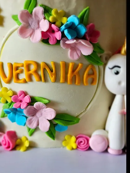 A detail shot of the unicorn cake, showing the personalized name and the cluster of tiny, handcrafted flowers that add texture and color to the design.