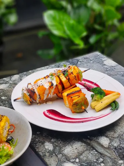 A delicious vegetarian meal of grilled paneer skewers, salad, and corn on the cob.