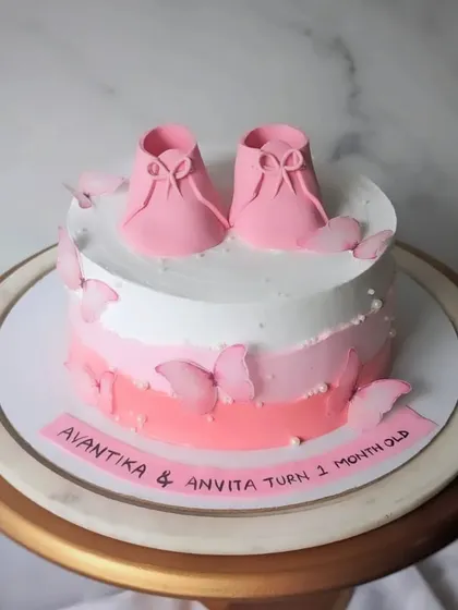 Celebrating one month of twin girls with this sweet pink cake. The design features two pairs of baby booties and a cascade of pink butterflies.