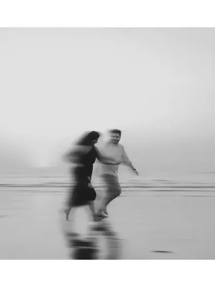 An artistic motion-blur shot in black and white. This image captures the feeling of a fleeting moment, a memory in motion as the couple walks along the shoreline.