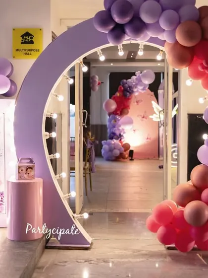 The entrance to Amayra's butterfly-themed party, featuring a lit-up welcome sign and a beautiful balloon arch in shades of purple and pink. The archway creates an inviting and exciting first impression.
