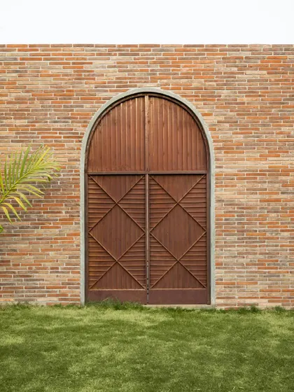 An arched wooden door set within an exposed brick wall at the Samavana wedding venue. This detail combines traditional forms and materials to create a rustic yet refined aesthetic.