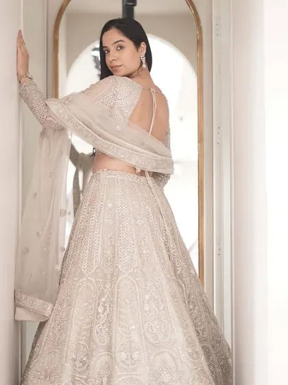 The back view of the ivory lehenga, showcasing its beautiful open-back blouse design and the continuation of the intricate embroidery.