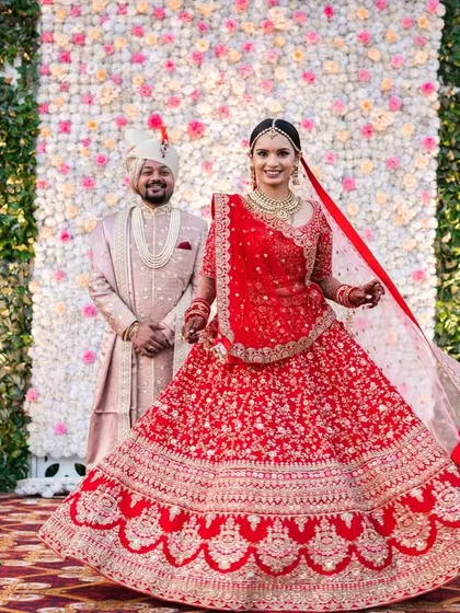 A beautiful twirl shot of the bride, showing off her magnificent red lehenga against the floral backdrop of the mandap.