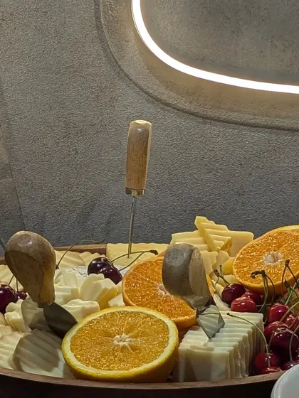 A close-up of a cheese board under modern neon lighting. The platter is filled with cherries, orange slices, and a variety of cheeses, showcasing a contemporary and trendy presentation.