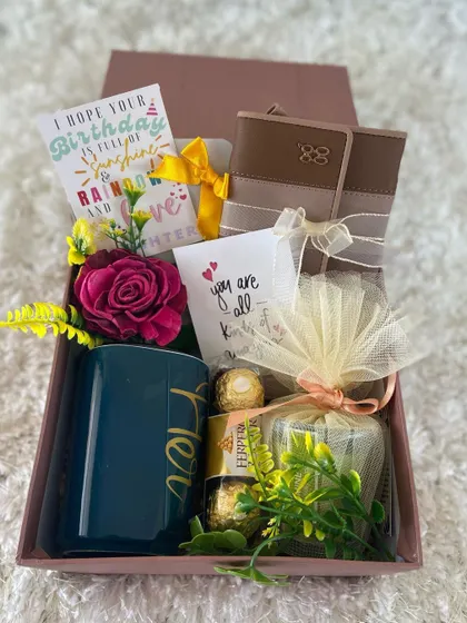A cheerful and elegant birthday gift box for her. This hamper features a "Her" mug, a wallet, Ferrero Rocher chocolates, a scented candle, and a lovely birthday card wishing a day full of sunshine, rainbows, and love.