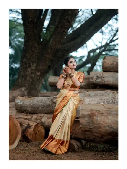 An elegant bridal portrait, with the bride posing against a rustic backdrop of stacked logs, her golden saree shining.