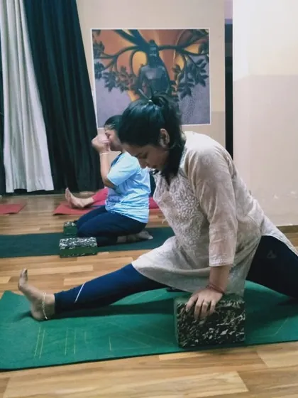 A student practices a supported front split in a group class. The shared journey of practice creates a motivational and encouraging environment for everyone to progress at their own pace.