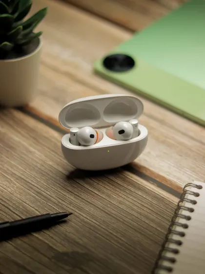 Another angle of the realme earbuds on a wooden desk, showing them next to a notebook and pen.