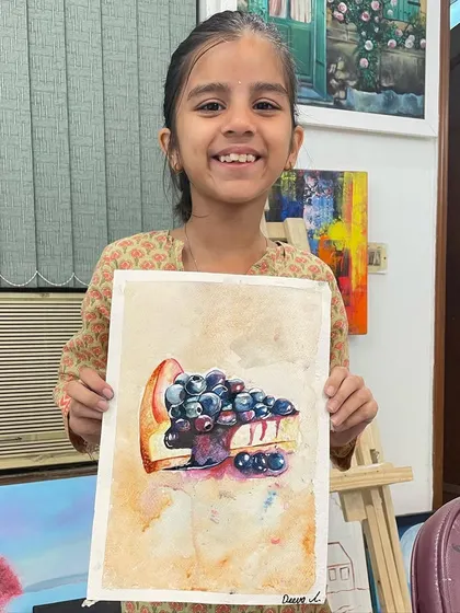 A young artist proudly displays her watercolor painting of a blueberry cheesecake. This was a fun project for learning how to paint different textures, from the glossy fruit to the crumbly crust.