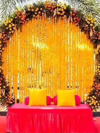 Our most requested Haldi backdrop design. A large ring of marigolds frames a curtain of genda strings, with a simple diwan for seating, perfect for any outdoor pre-wedding event.