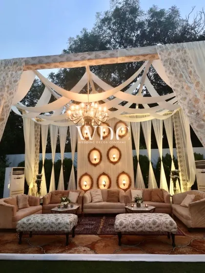 An outdoor lounge area designed with an ivory and gold theme. The setup features comfortable sofas, intricate drapes, and a beautiful chandelier, creating a regal and inviting space.