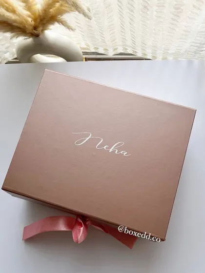 Personalization is key. This close-up shows a rose gold gift box elegantly customized with the bridesmaid's name, 'Neha', making the gift feel exclusive from the moment it's received.