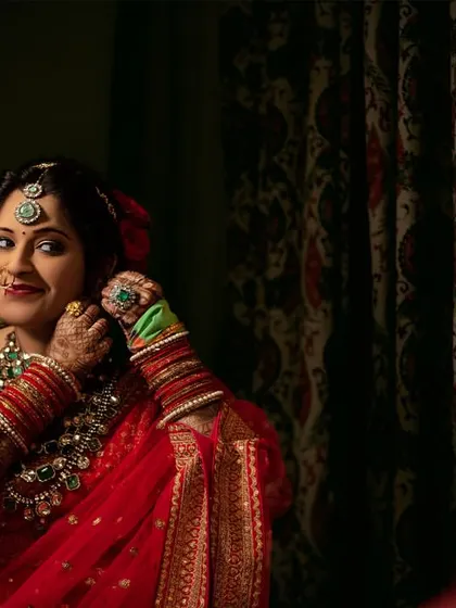 A moment of reflection. The bride, in her stunning red saree, adjusts her earring while looking in the mirror.