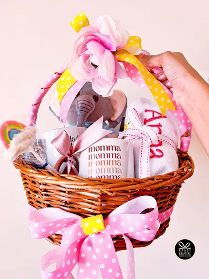 A beautifully decorated first birthday basket for a baby girl, complete with a personalized towel, 'Momma' mug, and colorful ribbons.